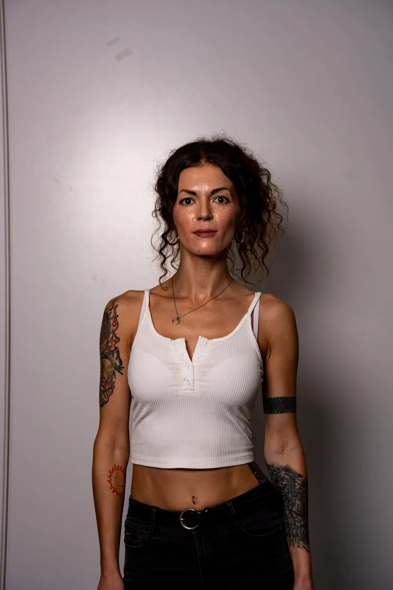 Una candidata de pelo rizado con top blanco y tatuajes en los brazos, de frente