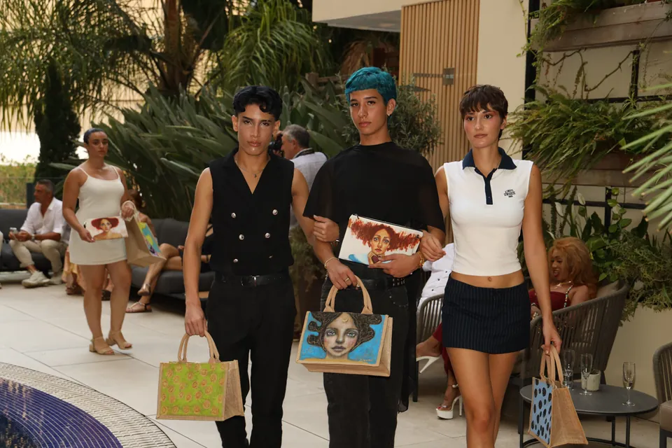 Drei Models laufen mit handbemalten Taschen vor dem Publikum, im Hotel Saratoga