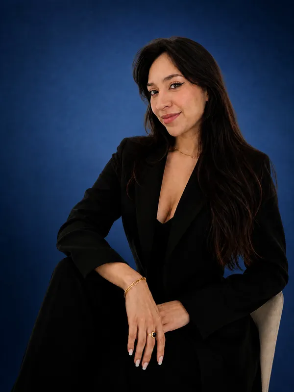 Nicolle Cantor in schwarzem Blazer, sitzend, vor blauem Studiohintergrund