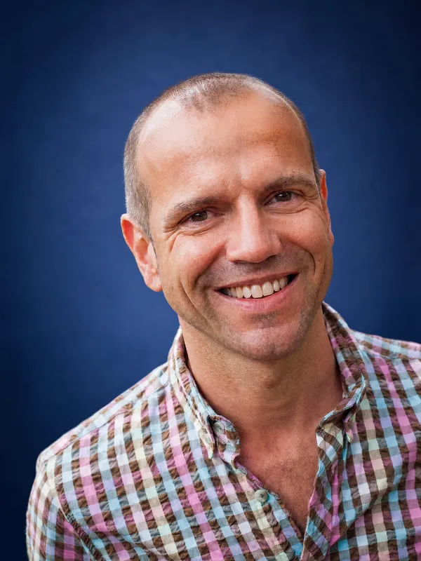 Philippe Salva, lächelnd, in kariertem Hemd vor blauem Studiohintergrund