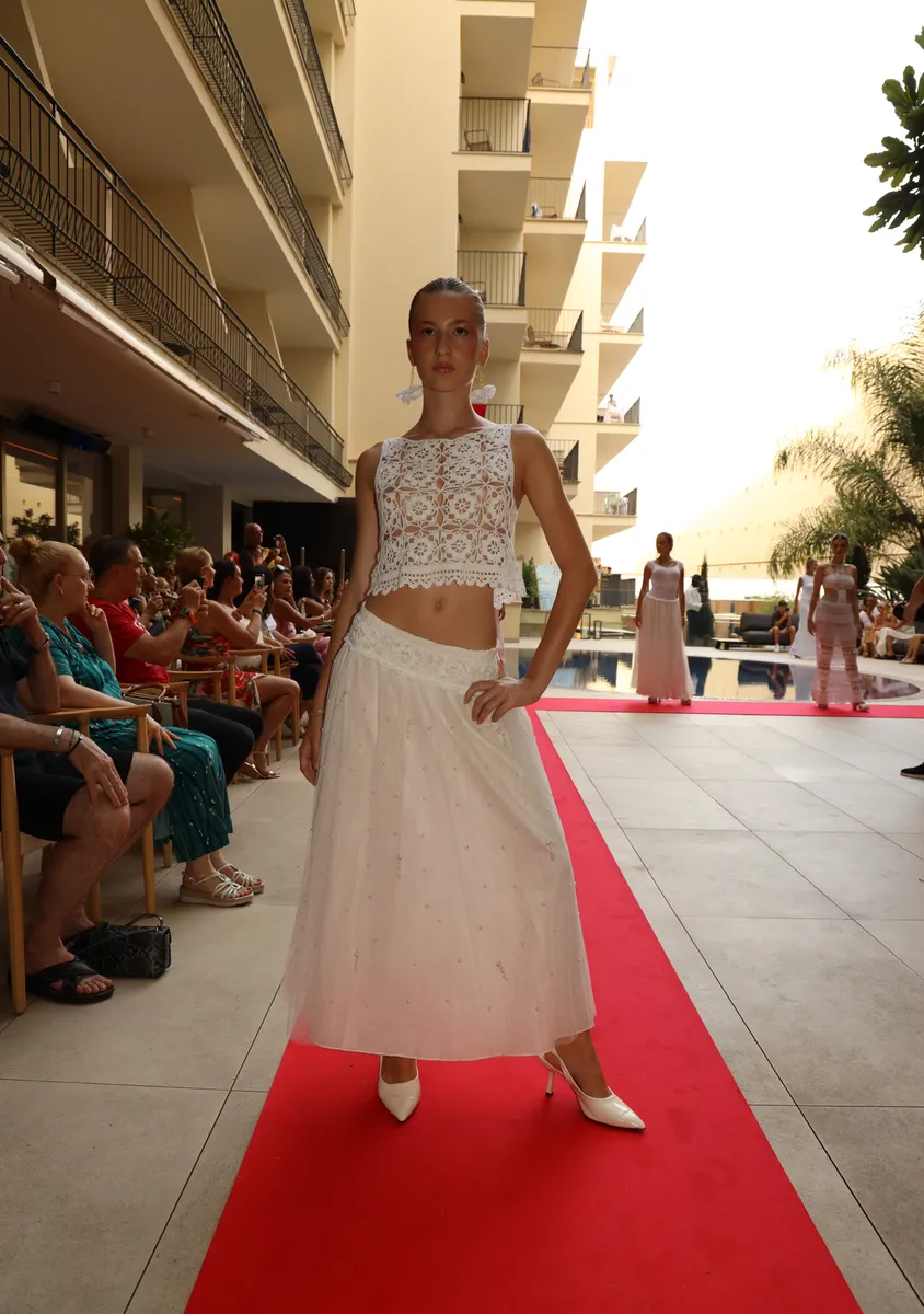 Una modelo con top de ganchillo y falda larga blanca en la alfombra roja del Hotel Saratoga, con público a un lado
