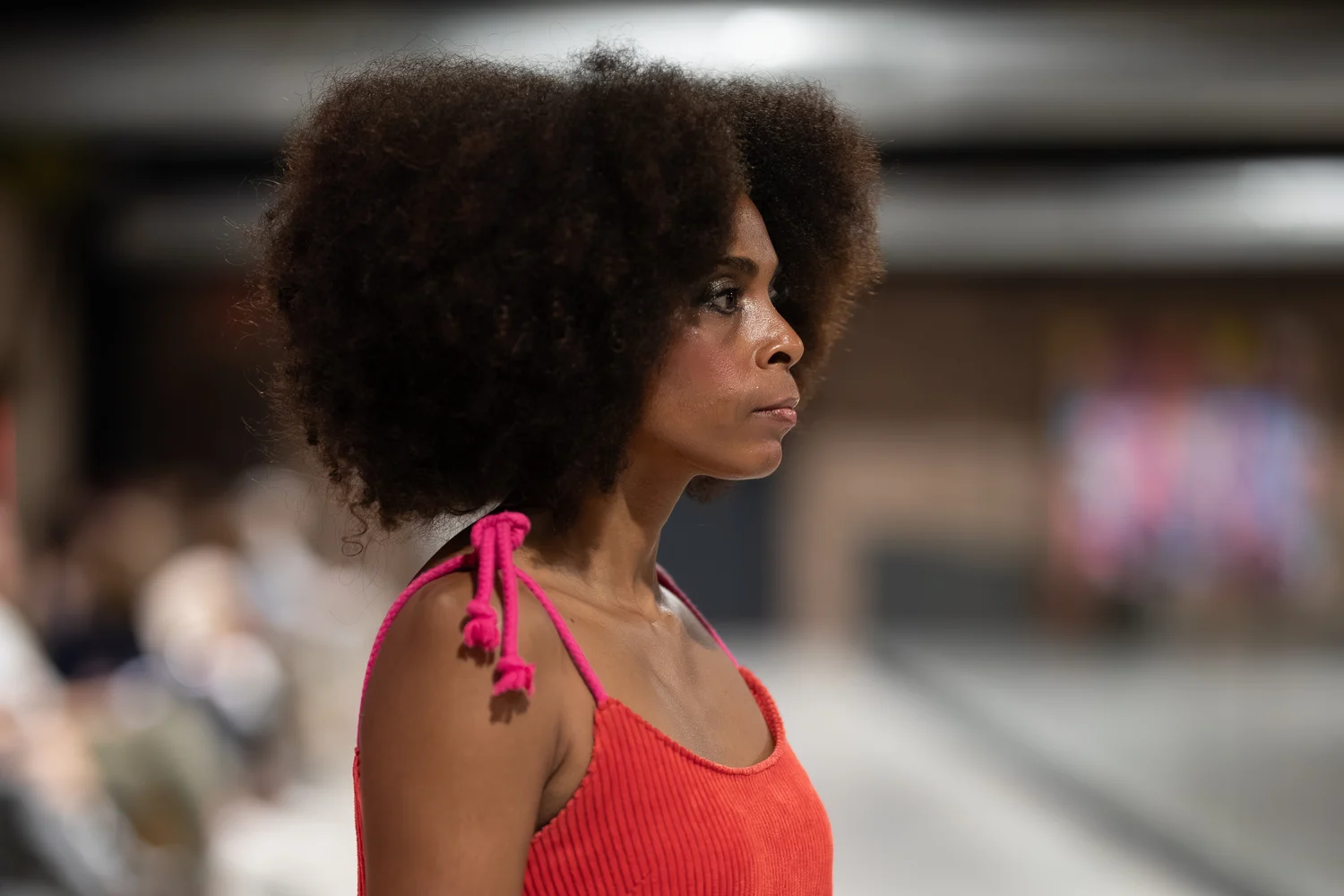 Ein Model im Profil, in einem korallenroten Rippentop mit pinkfarbenen Bändern an der Schulter, auf dem Laufsteg von Mallorca Fashion Days 2025, dahinter das Publikum