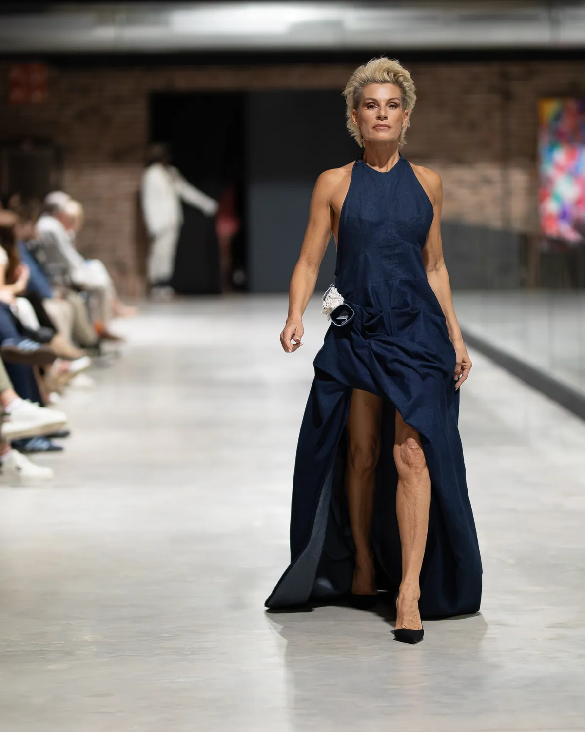 Ein Model in einem langen marineblauen Kleid läuft über den Laufsteg von Mallorca Fashion Days 2025, seitlich das sitzende Publikum