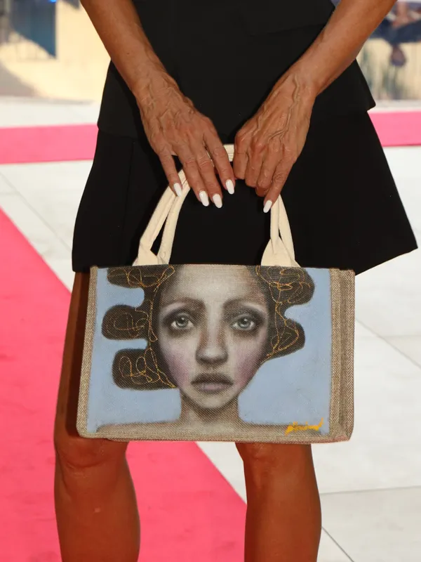Die Hände eines Models halten eine handbemalte Tasche mit dem Porträt einer Frau, bei der Modenschau im Hotel Saratoga